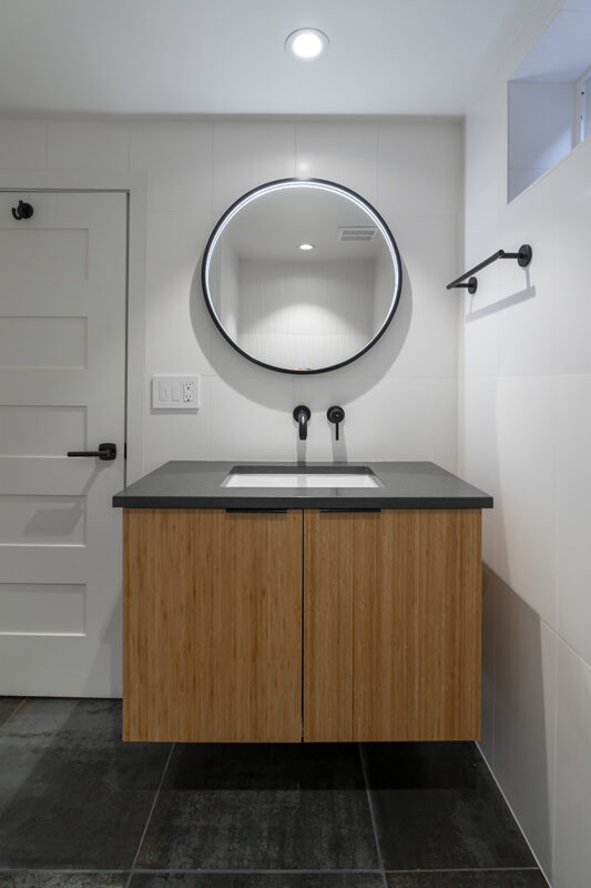 floating wood bathroom sink with black stone countertop and large circular LED mirror.