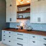 white cabinetry storing with wood countertops and multicolored hexagonal tile backsplash.