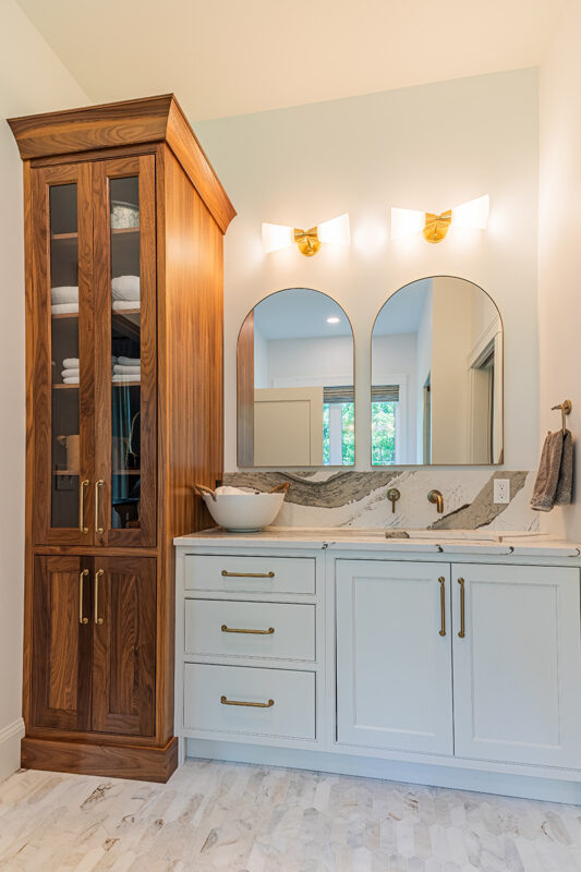 white bathroom vanity with brass accents accompanied by a tall wooden storage center