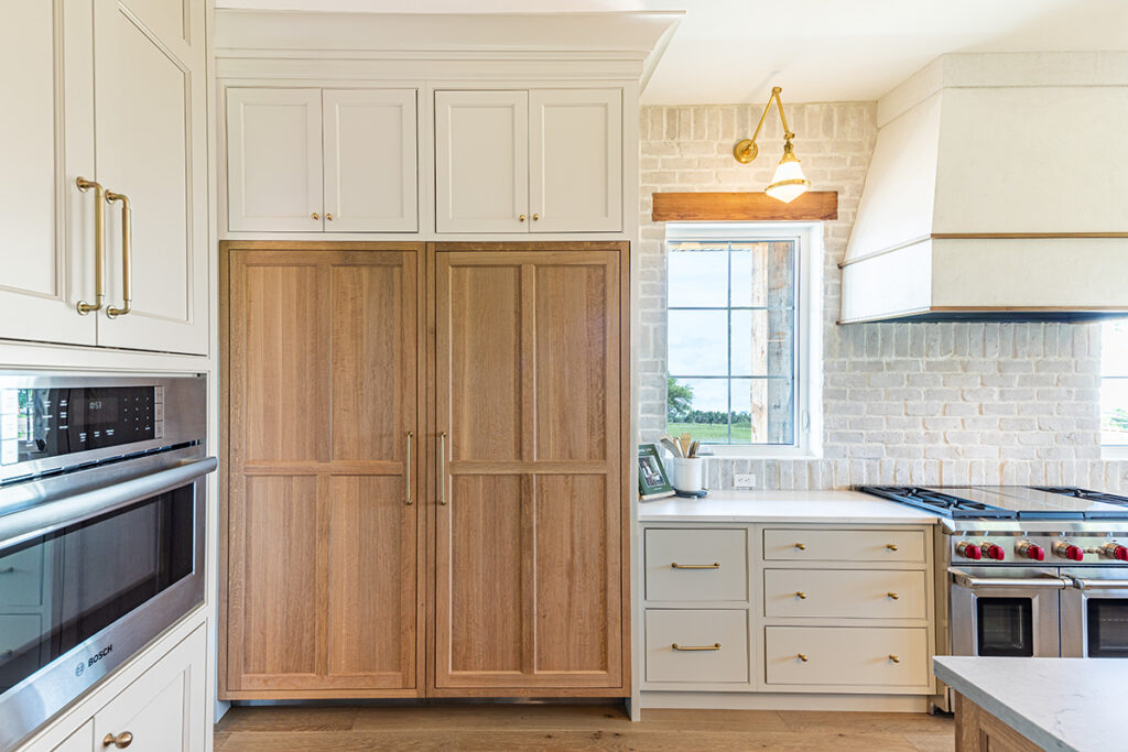 white wood kitchen with gold accents, dark wooden fridge, stainless steel appliances and stone backsplash