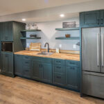 teal wooden cabinetry with stainless steel fridge. Light brown wooden countertops.