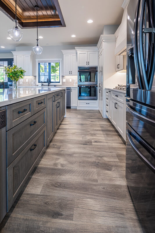 White kitchen cabinetry with black accents. Brushed wooden floor and modern light fixtures.