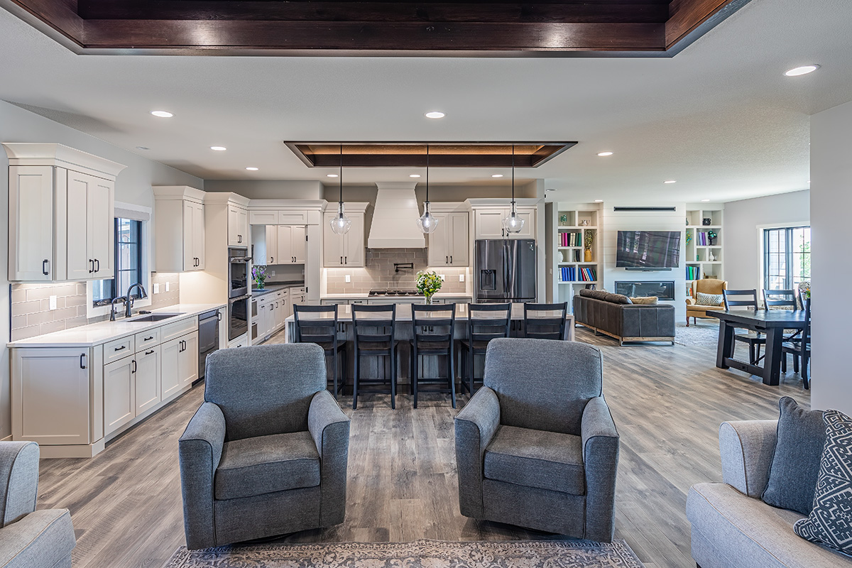 Shows a wide-angle view of the living spaces including a kitchen, dining space, and two sitting areas. The space is cohesive with white cabinets and color scheme.
