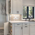 white kitchen cabinetry with spice cabinets. Glossy stone backsplash above the cabinetry.
