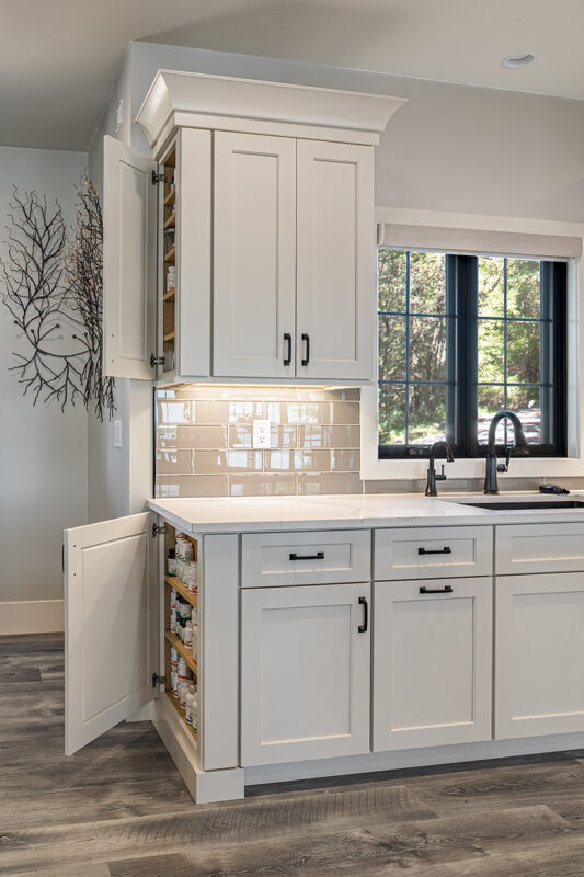 white kitchen cabinetry with spice cabinets. Glossy stone backsplash above the cabinetry.