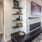 electric fireplace surrounded by stone. the attached wooden shelving unit is holding books and pictures.