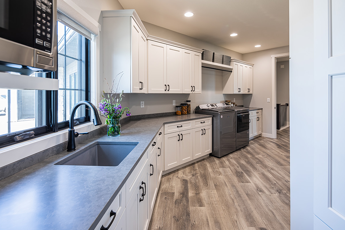 grey countertops with white cabinets. the floor is a brushed grey natural wood. this kitchen shows a layout for built in washer & dryer in the kitchen space.