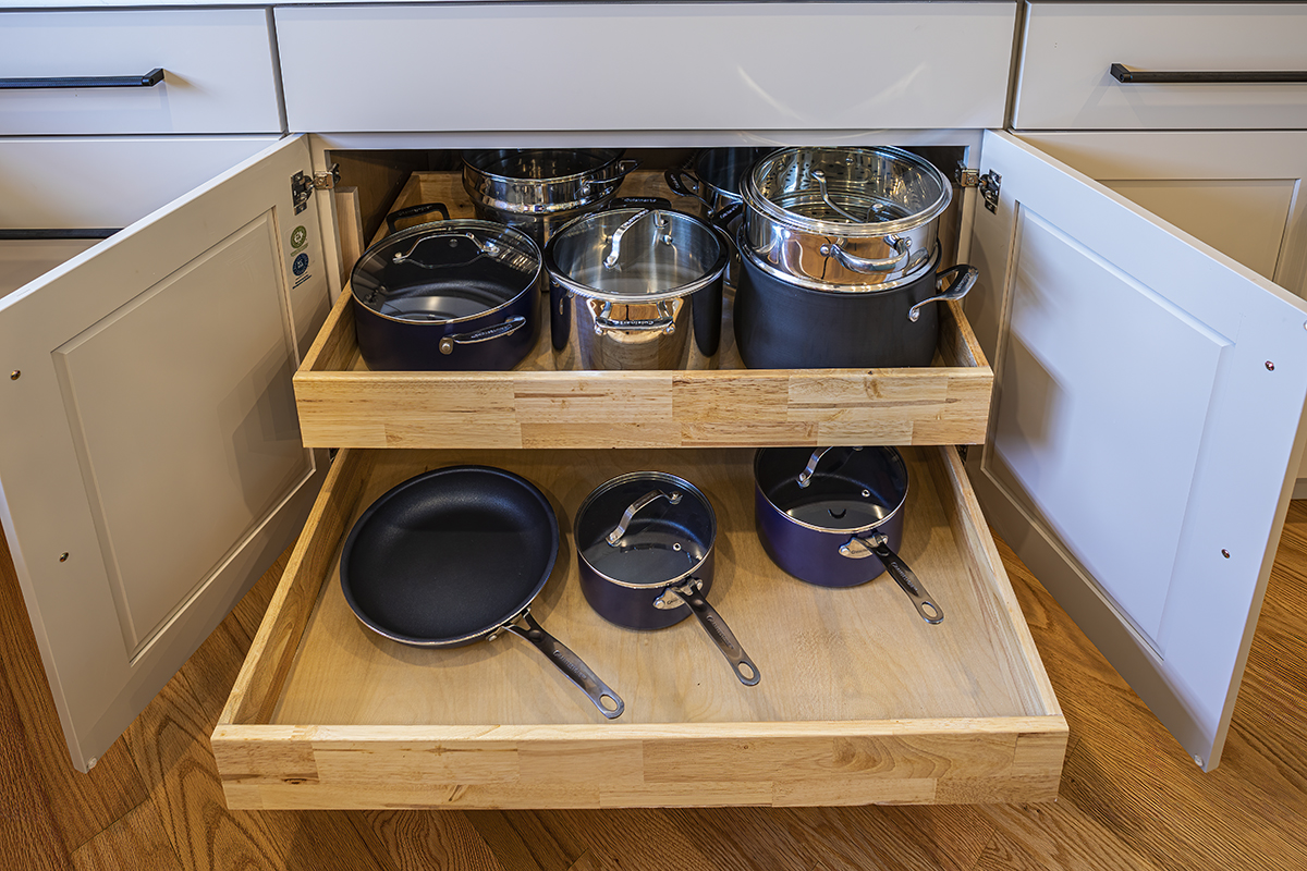 pots and pans inside white kitchen cabinets, drawers pulled outward.