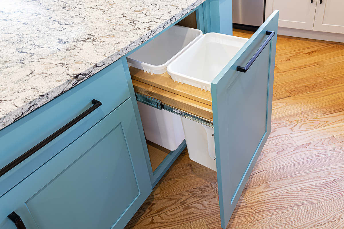 A blue kitchen cabinet with a trash can in it.