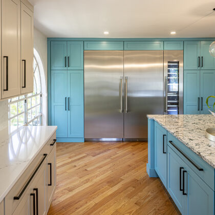 Dual tone kitchen with teal blue cabinets and marble counter tops. Half of the kitchen is teal blue, the other half of the kitchen is beige. The black handles remain consistent throughout.