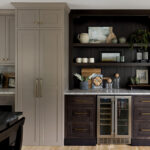 Stained home bar with wine cooler next to painted kitchen cabinets