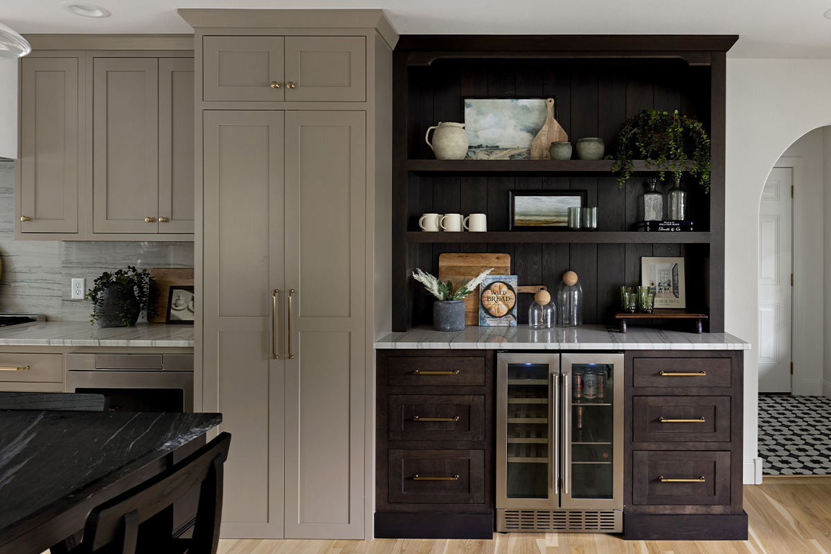 Stained home bar with wine cooler next to painted kitchen cabinets