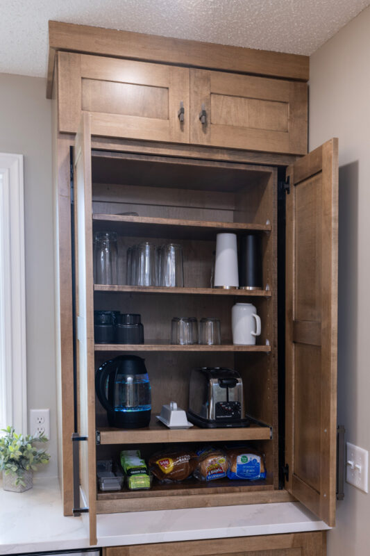 Beverage center cabinet with pocket doors hiding appliances, cups and mugs.