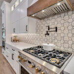 White kitchen with stained accent posts on island and apron on hood. Up close view of gas stove with pot filling faucet.