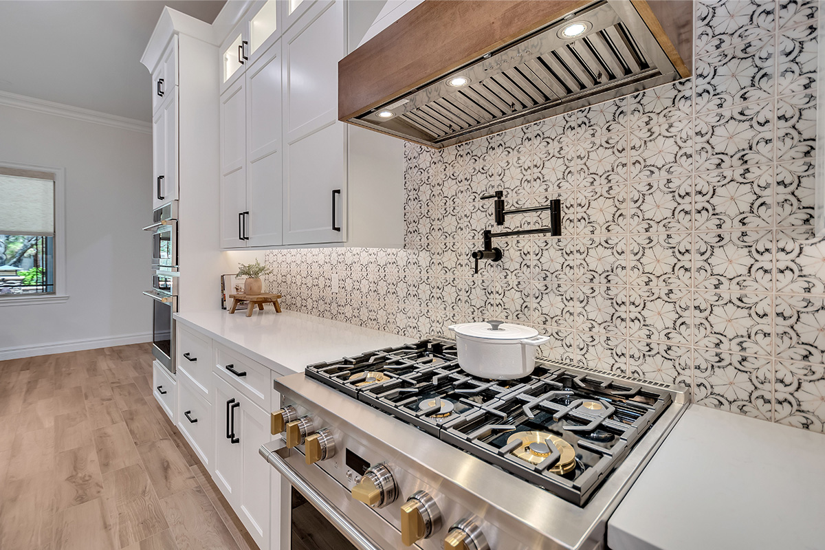 White kitchen with stained accent posts on island and apron on hood. Up close view of gas stove with pot filling faucet.