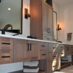 Stained bathroom vanity cabinets with open shelf on the bottom and a countertop wall cabinet splitting 2 sinks