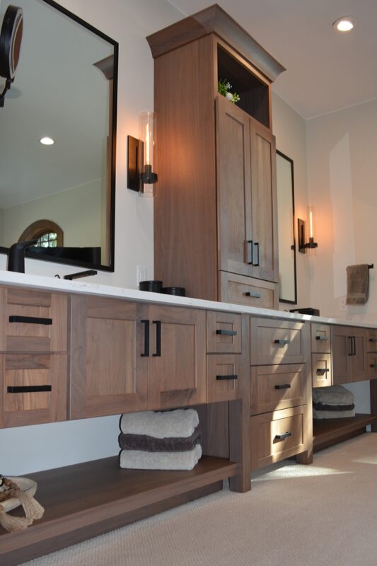 Stained bathroom vanity cabinets with open shelf on the bottom and a countertop wall cabinet splitting 2 sinks