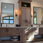 Stained bathroom vanity cabinets with open shelf on the bottom and a countertop wall cabinet splitting 2 sinks