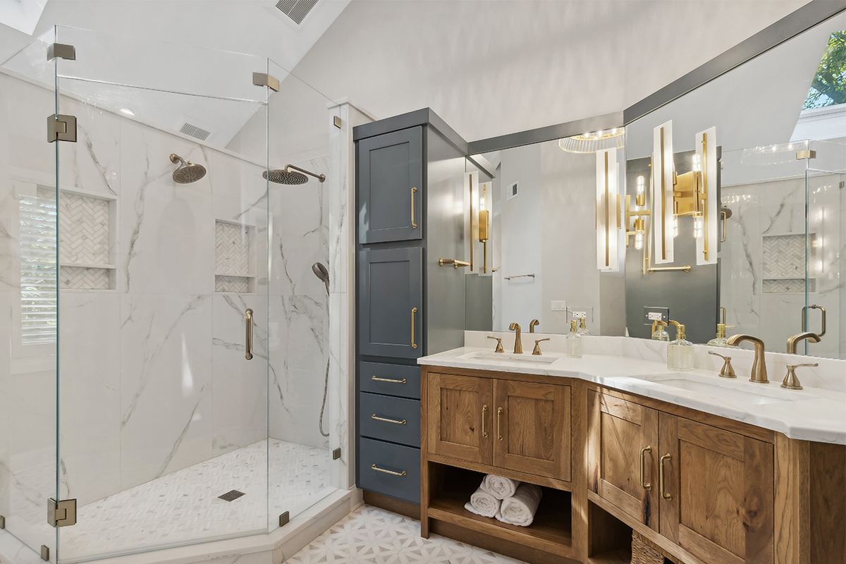 Master bathroom with stained vanity cabinets and painted tall linen cabinets. Also includes a shower with glass walls.