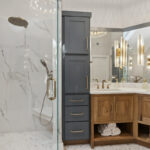 Master bathroom with stained vanity cabinets and painted tall linen cabinets. Also includes a shower with glass walls.