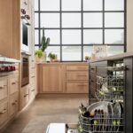 View of an open dishwasher in a stained and painted kitchen with a large window in the background