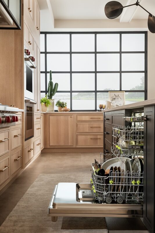 View of an open dishwasher in a stained and painted kitchen with a large window in the background