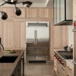 View of stained and painted kitchen cabinets with a large fridge in the distance