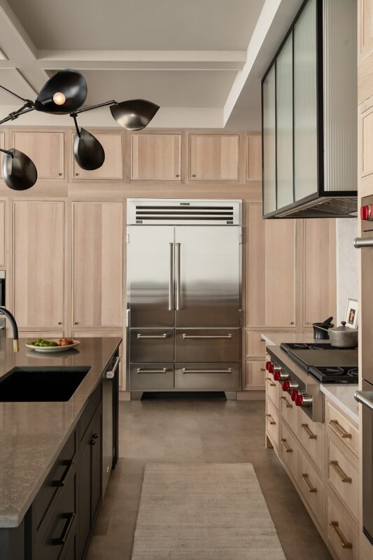 View of stained and painted kitchen cabinets with a large fridge in the distance