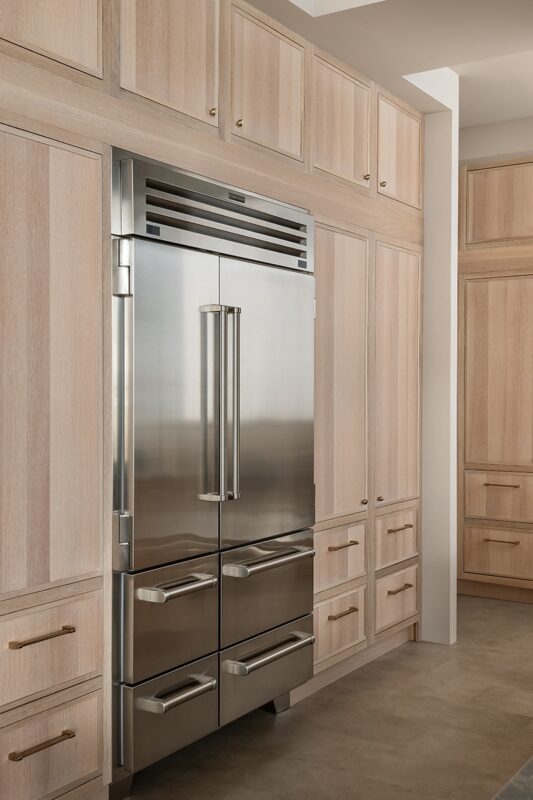 View of stained and painted kitchen cabinets with a large fridge