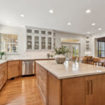 Light brown stained kitchen cabinets and white painted accent cabinets with glass door inserts.