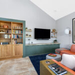 Living room space with painted green cabinets below a tv on the wall and stained white oak book cases to the left framed with green end panels.