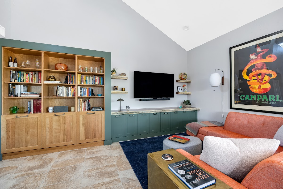 Living room space with painted green cabinets below a tv on the wall and stained white oak book cases to the left framed with green end panels.
