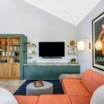 Living room space with painted green cabinets below a tv on the wall and stained white oak book cases to the left framed with green end panels.