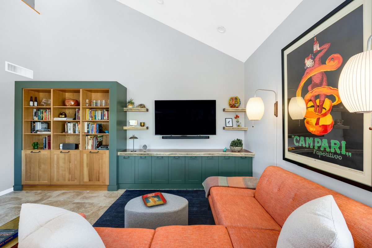 Living room space with painted green cabinets below a tv on the wall and stained white oak book cases to the left framed with green end panels.