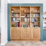 Living room space with painted green cabinets below a tv on the wall and stained white oak book cases to the left framed with green end panels.