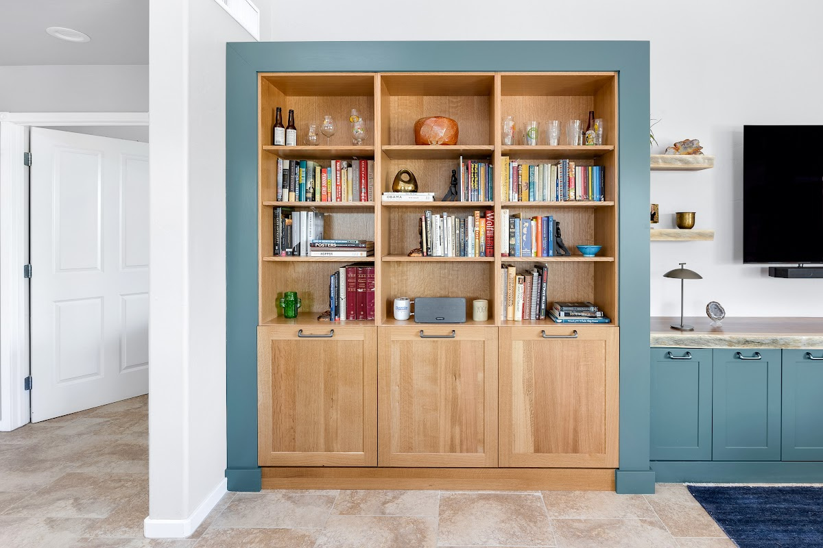 Living room space with painted green cabinets below a tv on the wall and stained white oak book cases to the left framed with green end panels.