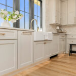 Painted and stained kitchen cabinets in a large open space with large windows.