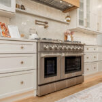 Painted and stained kitchen cabinets in a large open space with large windows.