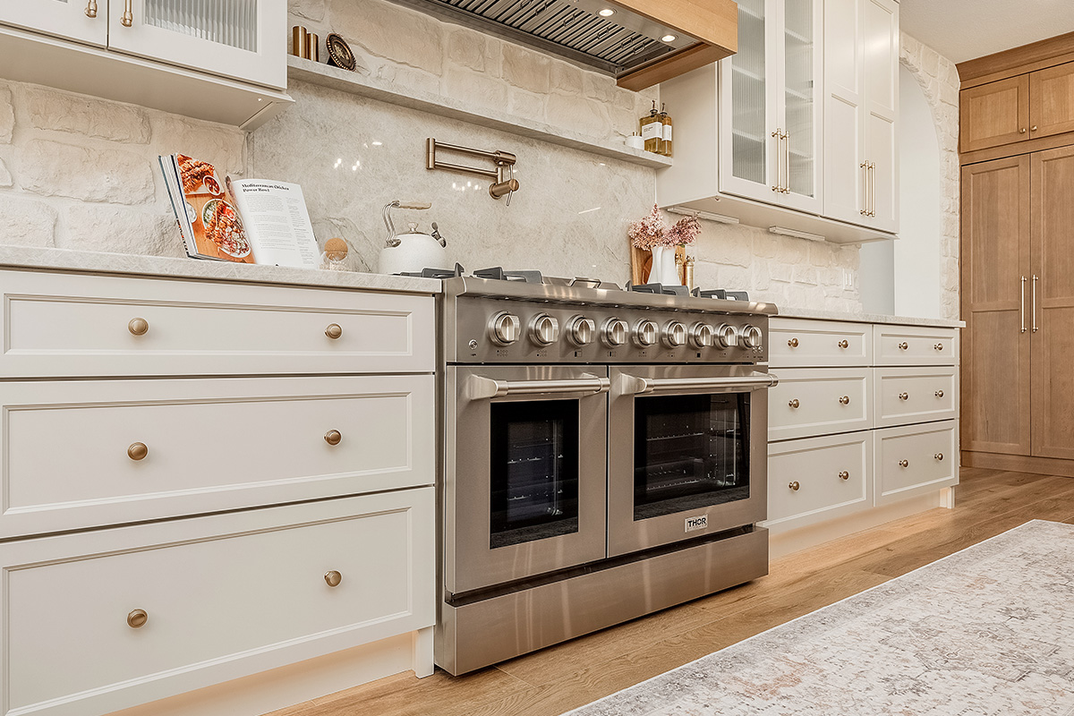 Painted and stained kitchen cabinets in a large open space with large windows.