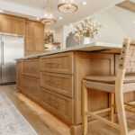 Painted and stained kitchen cabinets in a large open space with large windows.