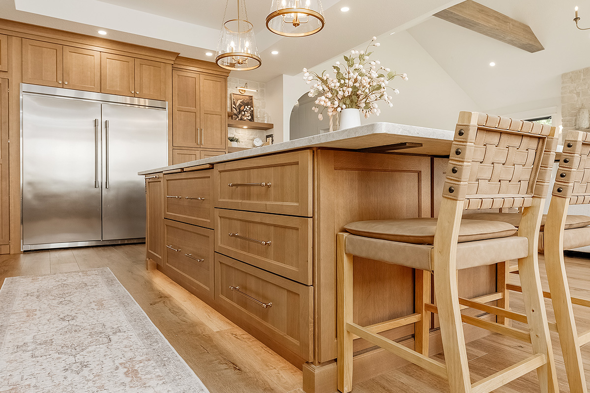 Painted and stained kitchen cabinets in a large open space with large windows.