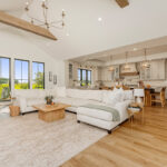 Painted and stained kitchen cabinets in a large open space with large windows viewed from the living room with high ceilings.