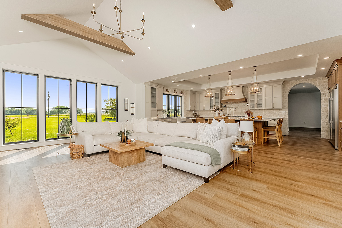 Painted and stained kitchen cabinets in a large open space with large windows viewed from the living room with high ceilings.
