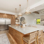 Painted and stained kitchen cabinets in a large open space with large windows.