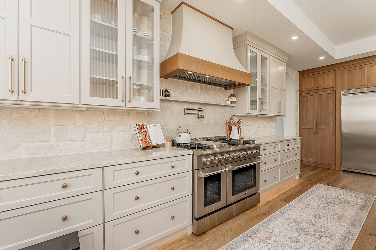 Painted and stained kitchen cabinets in a large open space with large windows.