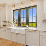 Painted and stained kitchen cabinets in a large open space with large windows.