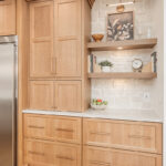 Painted and stained kitchen cabinets in a large open space with large windows.