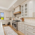 Painted and stained kitchen cabinets in a large open space with large windows.