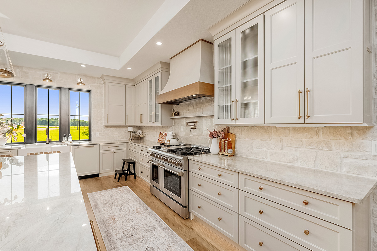 Painted and stained kitchen cabinets in a large open space with large windows.