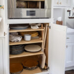 White painted kitchen cabinets with doors open showing shelves with baking dishes under an oven.